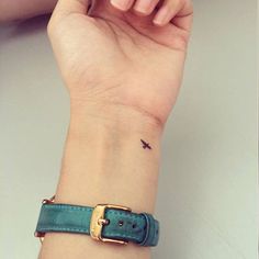 a woman's wrist with a small bird tattoo on the left side of her arm