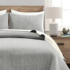 a bed in a bedroom with grey and white linens on the comforter, pillows and lamps