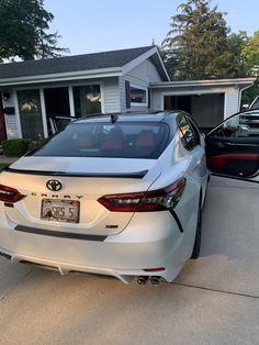 the rear end of a white car parked in front of a house with two other cars