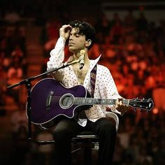 a man sitting on top of a chair holding a guitar in front of a microphone