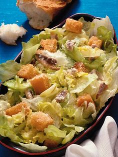 a salad with croutons and dressing in a red bowl on a blue table