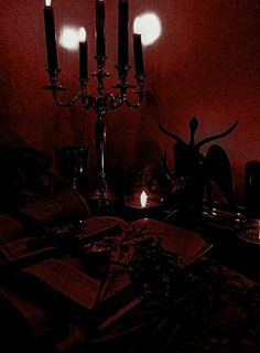 a table topped with candles and books in front of a red wall, next to a candelabra