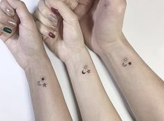 three women with matching wrist tattoos holding their hands up to the sky and stars on their wrists