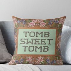 a cross stitch pillow with the words tomb sweet tomb on it, sitting on a couch