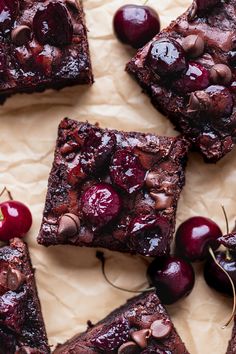 brownies with cherries and chocolate chips on parchment paper next to fresh cherries