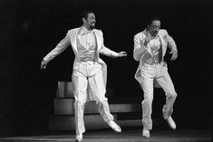 two men in white tuxedos are dancing on stage