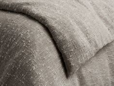 a close up view of a bed with a gray blanket and pillow on top of it