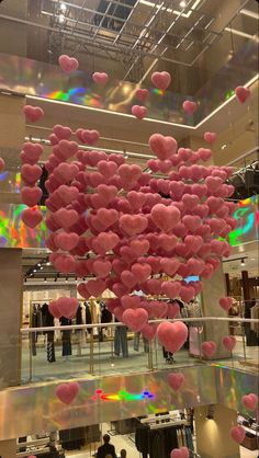 pink heart balloons floating from the ceiling in a shopping mall with people looking at them