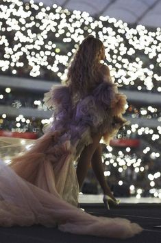 a woman in a dress is sitting on the ground with lights behind her and she has long hair