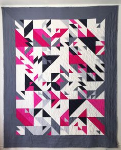 a pink and black quilt hanging on a wall next to a white wall with a gray border