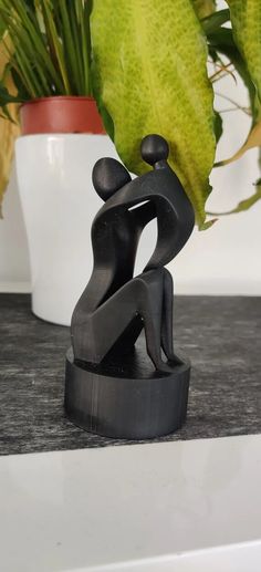 a black sculpture sitting on top of a counter next to a potted plant