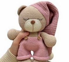 a crocheted teddy bear in pink and beige is held by someone's hand