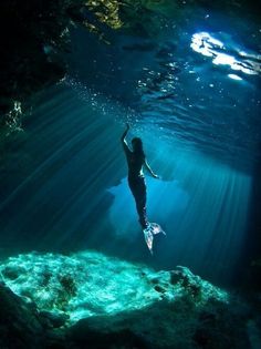 a woman is swimming in the ocean with her arms up and feet above water's surface