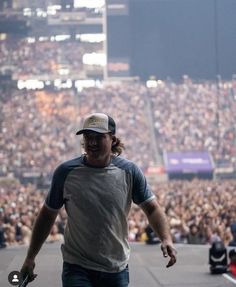 a man walking on top of a stage with a microphone in his hand and an audience behind him