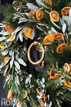 a wreath with oranges and greenery hanging from it's front door handle