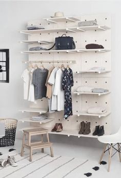 a white closet with clothes and shoes hanging on the wall next to a wooden stool