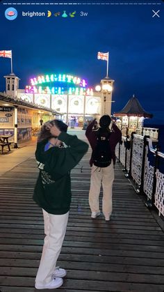 two people standing on a pier at night taking pictures with their cell phones and cameras