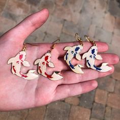 a person's hand holding five different colored fish earrings