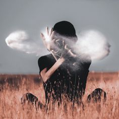 a person sitting in a field with their hands out to the sky and blowing white dust