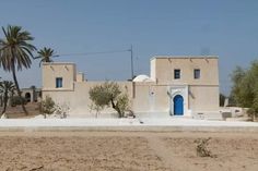 an adobe style house with blue door and windows in the desert, near palm trees