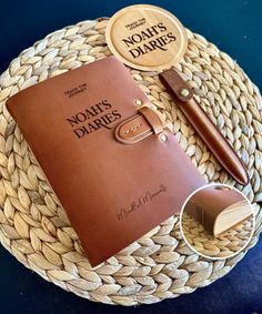 a brown leather bound notebook sitting on top of a woven basket next to a pen