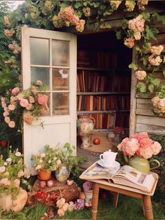 an open book sitting on top of a table next to flowers and bookshelves