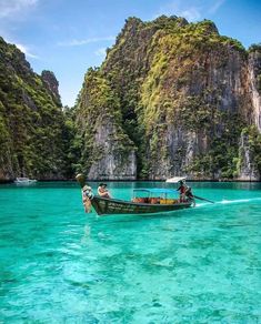 two people on a boat in the clear blue water near some mountains and cliffs,