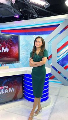 a woman is standing in front of a news set with her arms crossed and looking at the camera