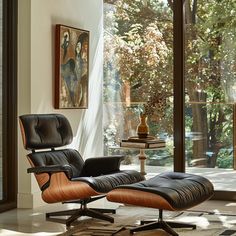 an eames lounge chair and ottoman in front of a large window with trees outside