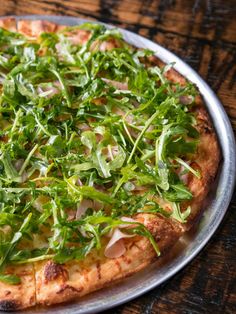 a pizza topped with greens on top of a metal pan