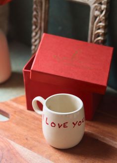 a coffee cup sitting on top of a wooden table next to a red box with the word love you written on it