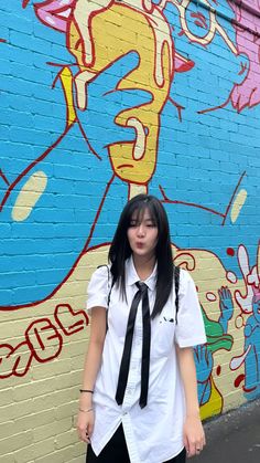 a young woman standing in front of a wall with graffiti on it's side