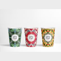 three paper cups with designs on them sitting side by side in front of a white background