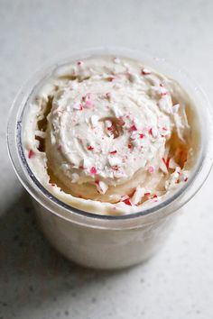 an ice cream with sprinkles in a plastic cup on a white surface