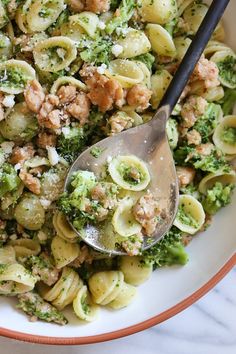 a bowl filled with pasta and broccoli on top of a marble countertop