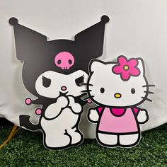 two hello kitty cut outs sitting next to each other on the ground with green grass