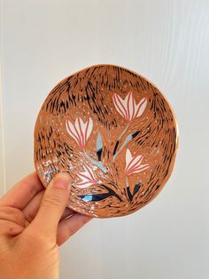 a hand holding a brown and pink plate with flowers on the inside, in front of a white wall