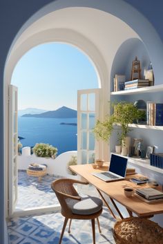 an arched window overlooks the water and blue sky, while a laptop sits on a desk