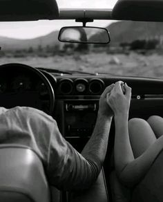 a man and woman sitting in the driver's seat of a car with their hands on the steering wheel