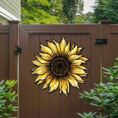 a sunflower is painted on the side of a brown fence with trees in the background