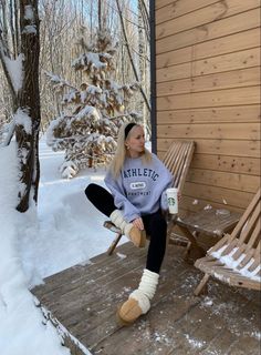 a woman sitting on a wooden bench next to snow covered trees and holding a bottle