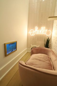 a pink couch sitting in front of a neon sign that says stella on the wall