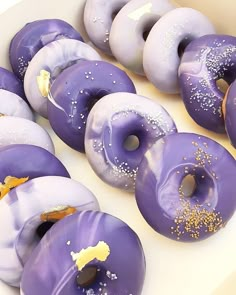 purple donuts with sprinkles and gold flakes in a white box