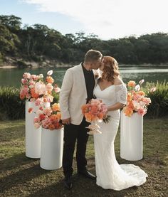 a bride and groom standing next to each other in front of tall vases with flowers