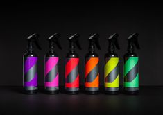 six spray bottles with different colors on them sitting next to each other in front of a black background