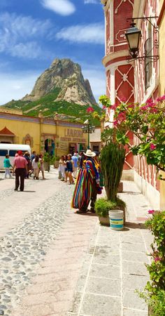 people walking down the street in front of a building with a mountain in the background