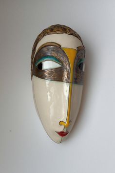 a white mask with gold and blue details on it's face, against a white background