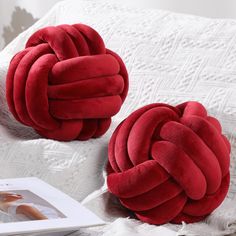 two red pillows sitting on top of a bed next to each other, one knoted