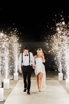 a bride and groom walking down the aisle with fireworks in the background