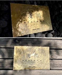 two gold cards with chinese writing on them sitting next to some rocks and pebbles in the background